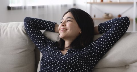 Close up Asian woman lean on couch relaxing put hands behind head open eyes looks into distance. Lazy day, admire view out the window, rented flat satisfied renter, enjoy air-conditioned air concept