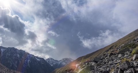 4k UHD timelapse of epic clouds in mountain valley at summer or autumn time. Wild endless nature and snow storm sky. Sun rays over snow summit. Fast movement
