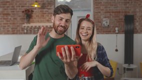 Happy couple uses smartphone video call with friends funny smiling stand at kitchen