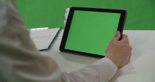 Medical worker woman in white coat using tablet over chroma key, green screen background. View over her shoulder. 4K RAW graded footage