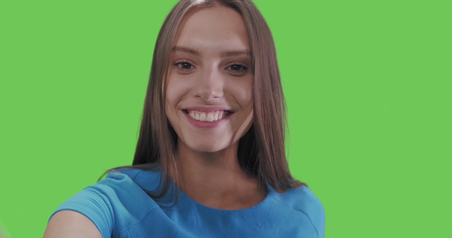 Young smiling woman in blue dress posing on green screen background. Girl taking selfie self portrait photo on smartphone. Chroma key. Female model showing positive face emotions. 4k raw video footage | Shutterstock HD Video #1055126240