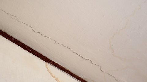 Water cracks on the plaster ceiling after heavy rain or leakage from the upper neighbor apartment. Large brown dirty spots on the plaster ceiling, water droplets destroying roof. Mold formation