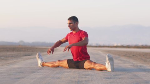 Athletic man stretching his legs and arms before working out outdoors at sunset