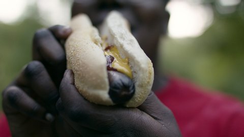 An African American woman take a big bite of a hot dog. Full of joy having a bbq with friends.