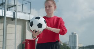 Teenager girl football soccer player doing ball tricks with her hands on rooftop empty parking garage. Urban city lifestyle outdoors concept. 4K UHD slow motion RAW graded footage
