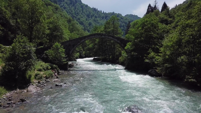 Rize city of Turkey.A very old stone bridge.A very strong river and a green forest.The drone camera goes up the river and passes under the bridge.