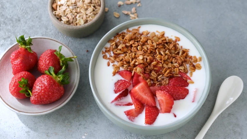 Yogurt with strawberry and granola. Slow motion of homemade granola falling in natural greek yogurt. Preparing healthy breakfast Royalty-Free Stock Footage #1055140835