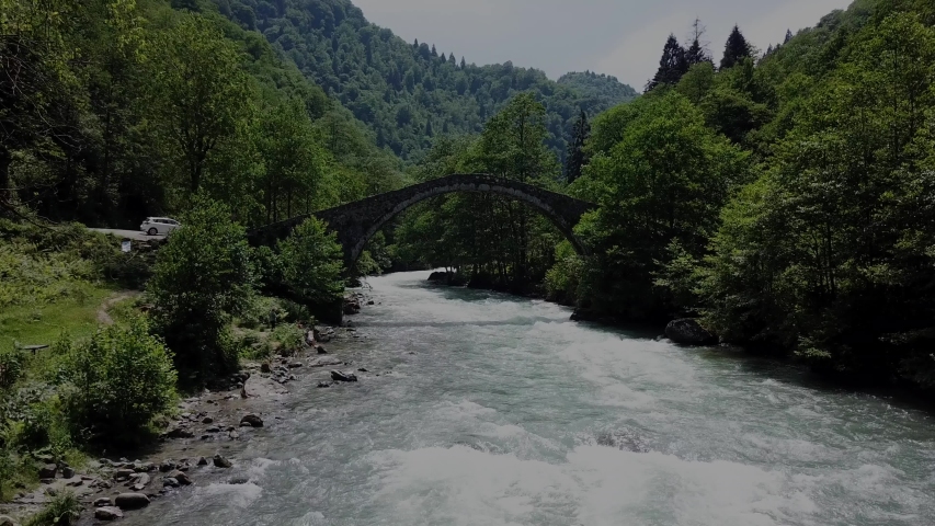 Rize city of Turkey.A very old stone bridge.A very strong river and a green forest.The drone camera is going up over the river.