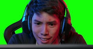Young asian pro cyber sport gamer vlogger in headset have live stream and playing in online video game on a computer with colourful UV lighting over green screen background.