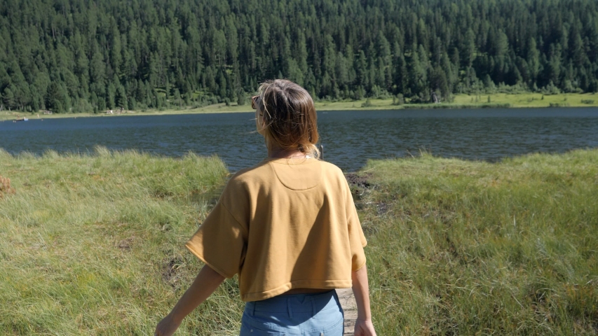 Woman walking on wooden pier above alpine lake, girl enjoying nature and fresh air from the mountains. Arms in the air