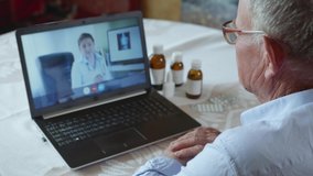 poor health, old male patient pensioner with glasses for vision consults doctor online on video call using modern technology, elderly man measures his pulse while sitting at table with laptop while
