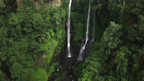 Downward zooming aerial shot of Sekumpul waterfalls - the best waterfalls in Bali. Breathtaking view of cascading waterfalls surrounded by a dense green tropical jungle.