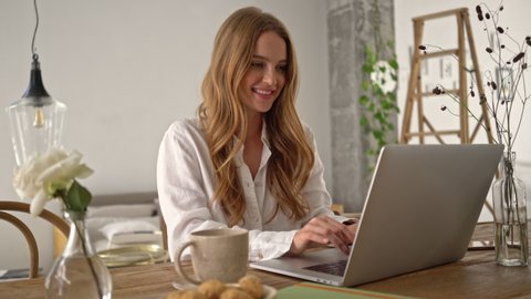 A cute young woman is typing on her laptop computer during breakfast in a cozy room at home