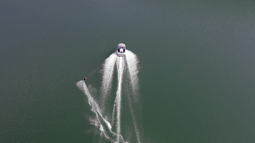 Aerial top view of a man water skiing on a lake in Austria. Dynamic action behind a speedboat with splashing water, showing balance, speed, and summer outdoor recreation.