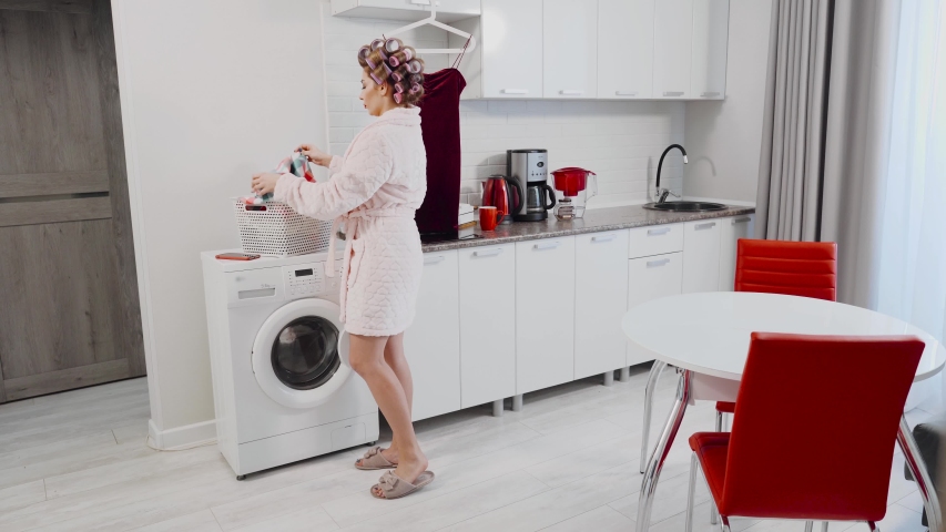 An agitated woman in a panic grabs the dress and wipes the water while the water flows from under the washing machine in the kitchen. A housewife who has a leak in the kitchen. Woman having washer Royalty-Free Stock Footage #1055149772