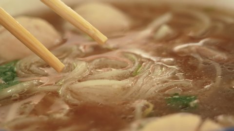 Close-up of hand use chopstick to pick noodles in a traditional Vietnamese beef soup Pho. Vietnamese style food.