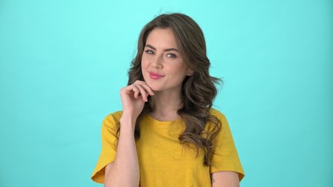 A beautiful young woman wearing yellow t-shirt is thinking or dreaming about something standing isolated over blue background