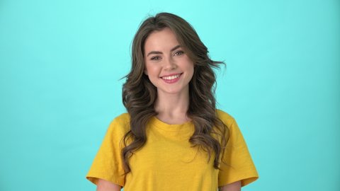 A smiling young woman wearing yellow t-shirt is nod positively to the camera standing isolated over blue background