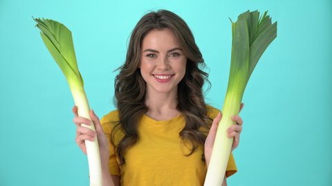 An attractive young woman wearing a yellow t-shirt is holding leek standing isolated over blue background