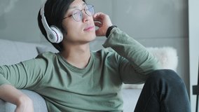 A relaxed young asian man with headphones enjoyed the music sitting in the living room at home