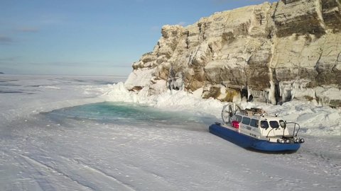 People travel on the ice of frozen Baikal Lake in a safe and comfortable Khivus hovercraft. Clip. Aerial view of the machine with air cushion bottom sliding on the melted ice of the frozen lake under