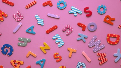 Colorful magnetic, plastic and paper alphabet letters placed randomly on pink background. Top view, flat lay.