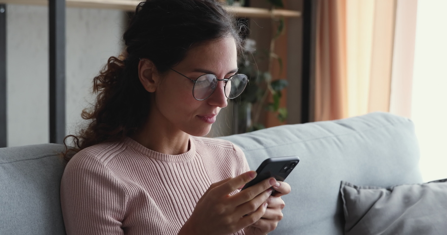 Head shot close up euphoric young attractive woman in eyeglasses looking at smartphone screen, reading sms with good news. Happy lady celebrating online game success or lottery win notification. Royalty-Free Stock Footage #1055154413