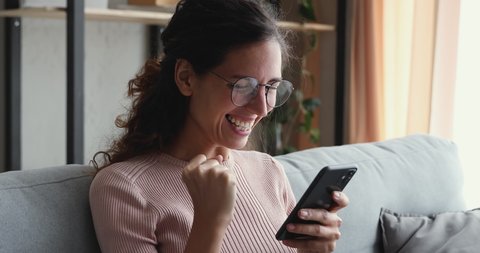 Head shot close up euphoric young attractive woman in eyeglasses looking at smartphone screen, reading sms with good news. Happy lady celebrating online game success or lottery win notification.