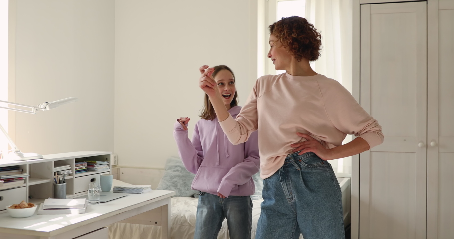 Happy mother giving dance lesson to smiling cute adolescent daughter at home. Overjoyed teen girl dancing to favorite energetic music, having fun with joyful mom indoors, family activities concept. Royalty-Free Stock Footage #1055154416