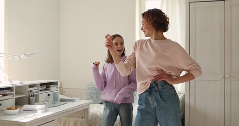 Happy mother giving dance lesson to smiling cute adolescent daughter at home. Overjoyed teen girl dancing to favorite energetic music, having fun with joyful mom indoors, family activities concept.