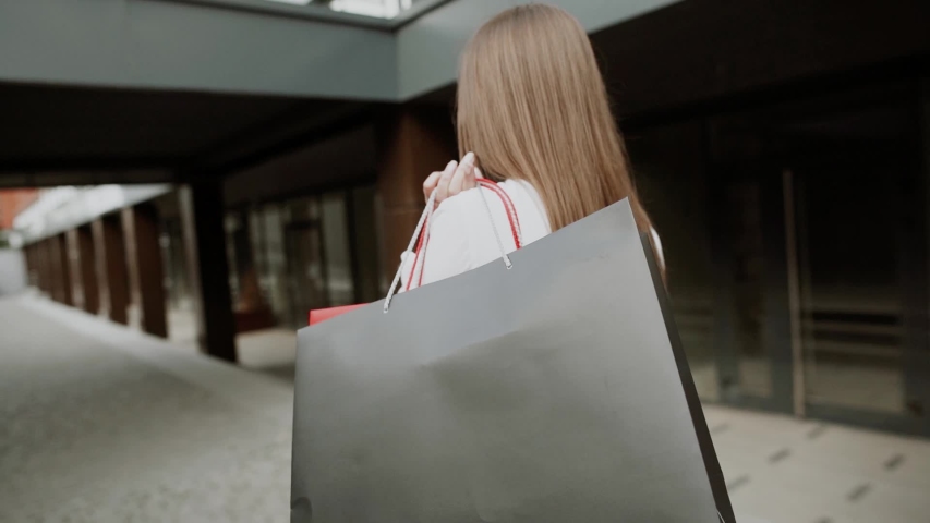 Young woman in red dress with shopping bags walks on the street during sunset