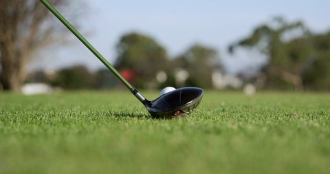 Low angle close up of golf club swinging and hitting a golf ball on a tee across a golf course, in slow motion