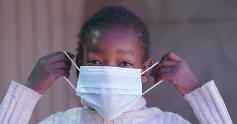 Poverty.Inequality. Cute young Black African girl puts on a face mask during lockdown to prevent Covid-19 Coronavirus pandemic, South Africa