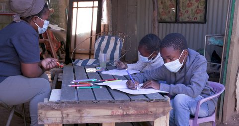 Poverty.Inequality.Black African woman home schooling her two young children at their dilapidated home during lockdown for Covid-19 Coronavirus pandemic, South Africa