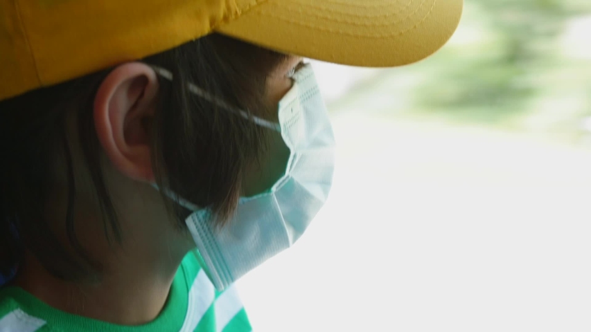 A child in a mask on his face looks out the window of the bus. Respiratory protection in a public place. Schoolboy on a bus during quarantine COVID-19. Royalty-Free Stock Footage #1055169215