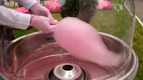 High angle of unrecognizable seller in gloves making pink cotton candy on machine in park