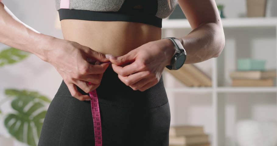 Close up shot of fit girl measuring her perfect waist. Female athlete losing extra weight after keeping a diet and doing sports - motivation concept 4k footage | Shutterstock HD Video #1055175149