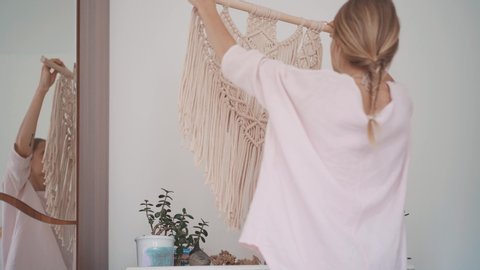 A young woman hang on the wall in a room with a diy fake colored cotton macrame mural on a wooden stick. Cozy interior in boho style and pastel colors.
Home plants mindfulness and organic inspiration