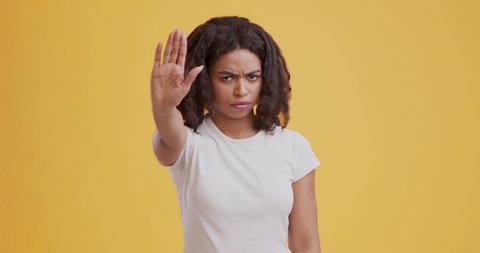 Portrait of serious african american girl making stop gesture with hand and shaking head as refusal, orange studio background