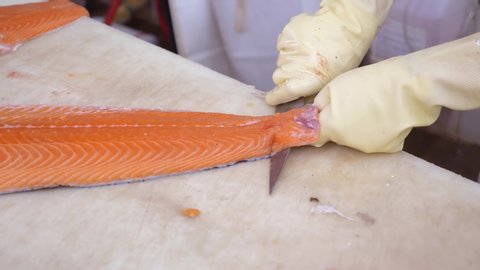 Close-up of Worker Hands Cutting and Cleaning Salmon Fillet from Skin by Big Chopping Knife in Grocery Store. Fresh Fish Clean and Cut Process in Supermarket