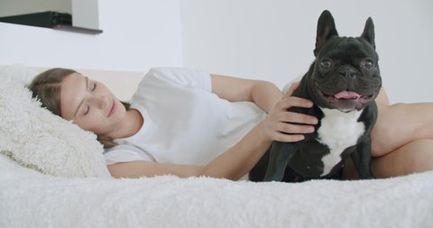 Attractive young woman and cute french bulldog dog are sleeping together at home on bed hugging enjoying relaxation. Humans and animals friendship concept. 4k raw video footage