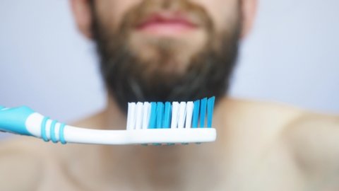 A young bearded man squeezes toothpaste onto a brush and brushes his teeth