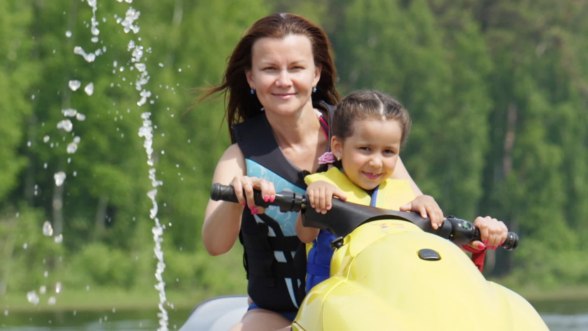 Mom and daughter ride the river on a personal watercraft, have fun and enjoy life. Sunny summer day. Slow motion Royalty-Free Stock Footage #1055181731