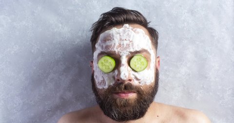 Brunette man with a beard in a spa salon gets clay facial mask with cucumbers on the eyes. Funny Stop motion animation