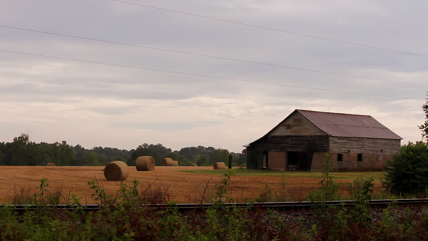 An old weathered barn in a golden field across train tracks with hay bales after a rain storm