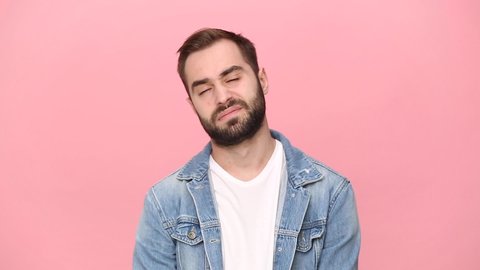 Sad exhausted boring bearded young guy 20s years old in denim jacket white t-shirt isolated on pastel pink background studio. People sincere emotions lifestyle concept. Looking at camera sigh suspire