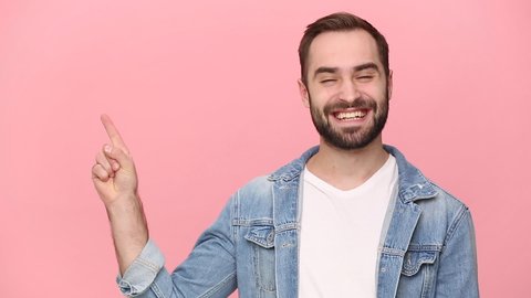 Happy bearded young man guy 20s years old in denim jacket white t-shirt isolated on pastel pink background studio. People lifestyle concept. Look camera pointing fingers hands on copy space workspace