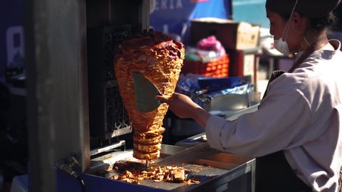 MEXICO CITY, MEXICO - DECEMBER 22, 2018: Masked cook prepares Mexican street tacos al pastor outdoors
