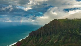 Inspiring nature 4K time-lapse background video. Massive clouds are flying above the famous Na Pali coastline revealing colorful rainbow over the ocean. Green Jurassic period forest at Kauai island