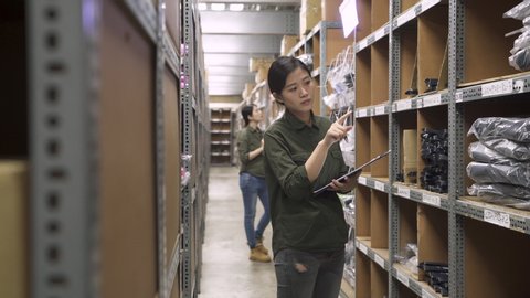 wholesale logistic people and export concept. asian korean woman supervisor with clipboards at warehouse stock taking with female colleague in blurred background walking. two coworkers in stockhouse